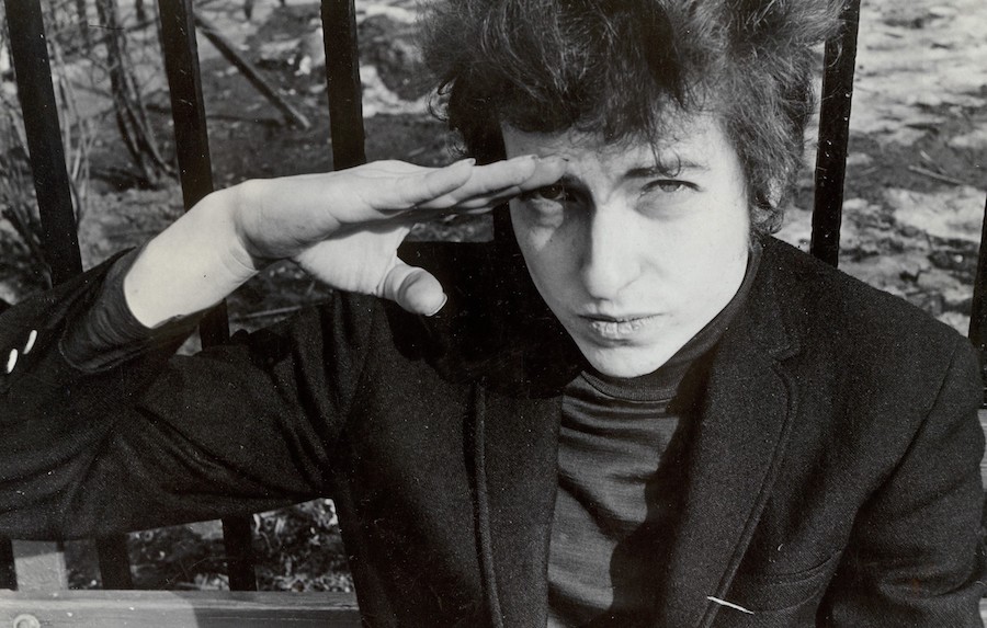 Fred W. McDarrah: Bob Dylan, sitting on a bench in Christopher Park (across the street from the offices of the Village Voice since 1960), either salutes or shields his eyes from the sun, January 22, 1965