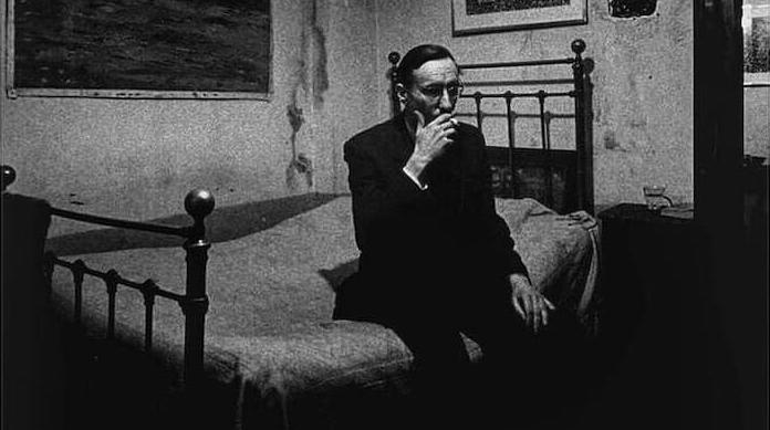 William S. Burroughs on a bed, smoking a cigarette.